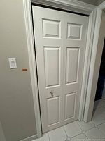 Closed white accordion closet door with paneled design in a beige/tan colored room.