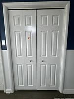 Front view of a set of two white accordion closet doors with paneled design and round knobs