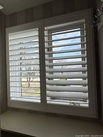 Full view of two connected white California shutter panels covering window, showing horizontal slats and overall condition