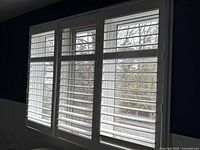 Three white plantation shutter panels installed in a window frame, showing horizontal slats and size relative to window space.