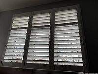 Three white shutter panels installed on a window, showing horizontal slats and overall coverage area.