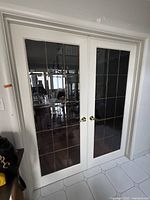 Front-facing clear image of both white French double doors showing gold hardware, window panes with gold trim, and white frame.