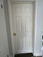 Front view of a white interior door with moulding detail showing gold knob hardware and hinge on the right side.