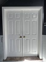 Front view of closed white interior double doors with gold handles, showing six panel design and door frame.