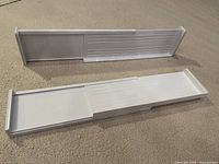 Photo of two white plastic adjustable drawer dividers on a beige carpet. Each divider has an extendable mechanism allowing length adjustment from approximately 13 to 23 inches.