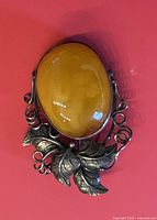 Close-up front view of an oval amber pendant set in a silver frame with decorative leaf and vine details.