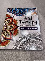 Front cover of the Art Therapy Coloring Book #2 showing mandala designs, some colored and some uncolored, with title text.
