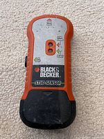 Orange and black handheld Black & Decker stud sensor device, shows front with labeling and sensor window.