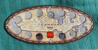 Oval display card showing 15 Canadian Millennium coins from 1999 in non-circulated condition, arranged evenly with a map and text background.