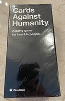 Photo of the Cards Against Humanity CA edition party game box, black with white text, showing front face with title and edition information.
