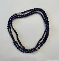 Blue beaded necklace displayed coiled on a white background showing full strand and clasp.