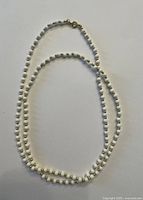 Photo of a white and gold bead costume jewelry necklace laid out on a plain background showing the entire length and clasp detail.
