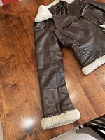 Brown leather jacket laid flat showing full sleeve and shearling cuff.