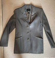 Front view of grey Danier leather blazer laid flat showing three buttons and two pockets.