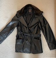 Front view of black leather coat laid flat showing fur collar, belt, pockets, and detailing.
