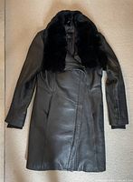 Full front view of black leather women's jacket with fur collar, laid flat
