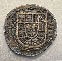 Front side of the gold cob doubloon replica showing heraldic crest with shields and fleur-de-lis.