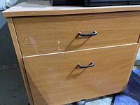 Front angle view of Ikea light wood laminate 2-drawer file cabinet showing metal handles and minor scuffs.
