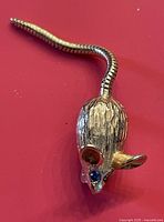 Metal mouse pin with one blue stone eye missing against a red background.