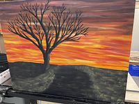 Photo of original painting showing a leafless tree silhouette against a vivid sunset sky, with colors in orange, yellow, and purple tones and a 38x30 inch canvas size.
