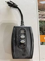 Photo showing a black outdoor outlet timer with digital display and two buttons, connected to a power plug.