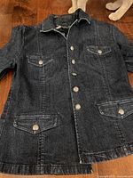 Front view of dark denim jean jacket with four flap button pockets and button front closure.