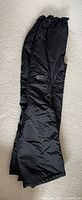 Full view of black Ripple Rock snow pants laid flat on carpet.