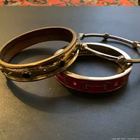 Three vintage condition bangles on black surface showing metal, enamel, and stone details
