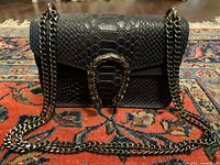 Front view of navy blue embossed leather handbag with chain strap on a patterned rug.