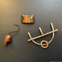 Photo showing three vintage brooches against black background: hand-painted portrait brooch, mouse-shaped wooden brooch, and abstract hammered metal brooch