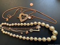 Overview of both necklaces showing the heart pendant with arrow and the faux pearl necklace with charms.