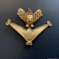 Close-up of vintage gold-tone brooch shaped like an abstract human figure with wing-like filigree