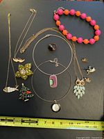 Various vintage necklaces and brooches arranged on black surface, including bead bracelet and different shaped pendants and brooches.