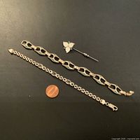 Three pieces on black background with penny for scale: two bracelets and one flower stick pin
