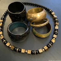 Overhead image showing five vintage costume bangles and a black and gold-tone beaded necklace arranged on a flat surface.