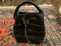 Front view of the black mini bag showing scalloped decorations and drawstring tied in a bow.