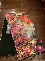 Overall view of multicolor silk scarf with black knit backing and fringe, water bottle for scale