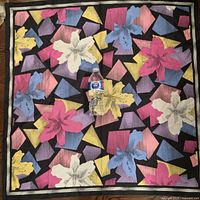 Front view of the entire scarf laid flat with a bottle placed for size reference, showing vibrant floral and geometric patterns on black background.