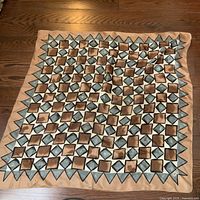 Silk scarf laid flat on wooden floor showing full pattern of alternating brown and gray diamond shapes on beige background.