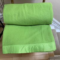 Full view of the apple green wool blanket rolled and laid flat, showing texture and satin binding on one end.