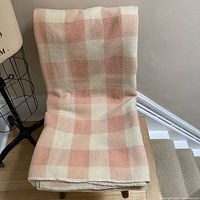 Pink and cream checkered wool blanket folded over a chair showing the large square pattern and soft texture.