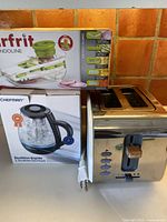 Three kitchen appliances together showing Starfrit Mandoline slicer box, Chefman kettle box, stainless steel two-slice toaster