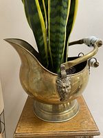 Side view of brass vessel with Delft ceramic handle grip, showing curved spout and overall form.