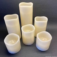 Six white wax battery operated candles grouped together, unlit, showing size variation and condition.