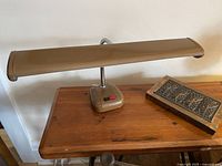 Metal gooseneck articulating desk lamp on wooden surface with shade closed.