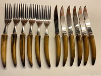 Full set of 6 serrated knives and 6 dinner forks arranged side by side, showing caramel to dark brown Bakelite handles and shiny stainless steel blades/tines.