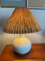 Lamp illuminated showing the pleated textured lampshade and cream ceramic base