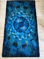 Full view of the rectangular mid-century wool carpet showing concentric circular and geometric pattern in blues, greens, and black on a light wood floor.