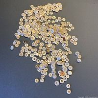 Overview of assorted mother of pearl buttons scattered on grey background, showing variety in size and color.