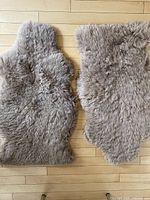 Top view of two pale grey sheepskin rugs laid flat, showing full rugs with fluffy wool surface.
